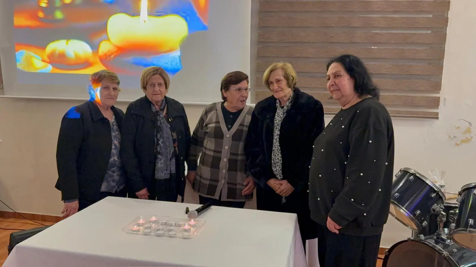 Five women of the church standing behind a table of lit candles during a candlelight service
