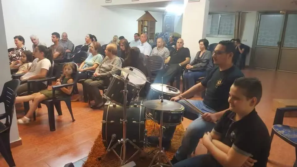 A young drummer playing during worship while children and families watch in the church room