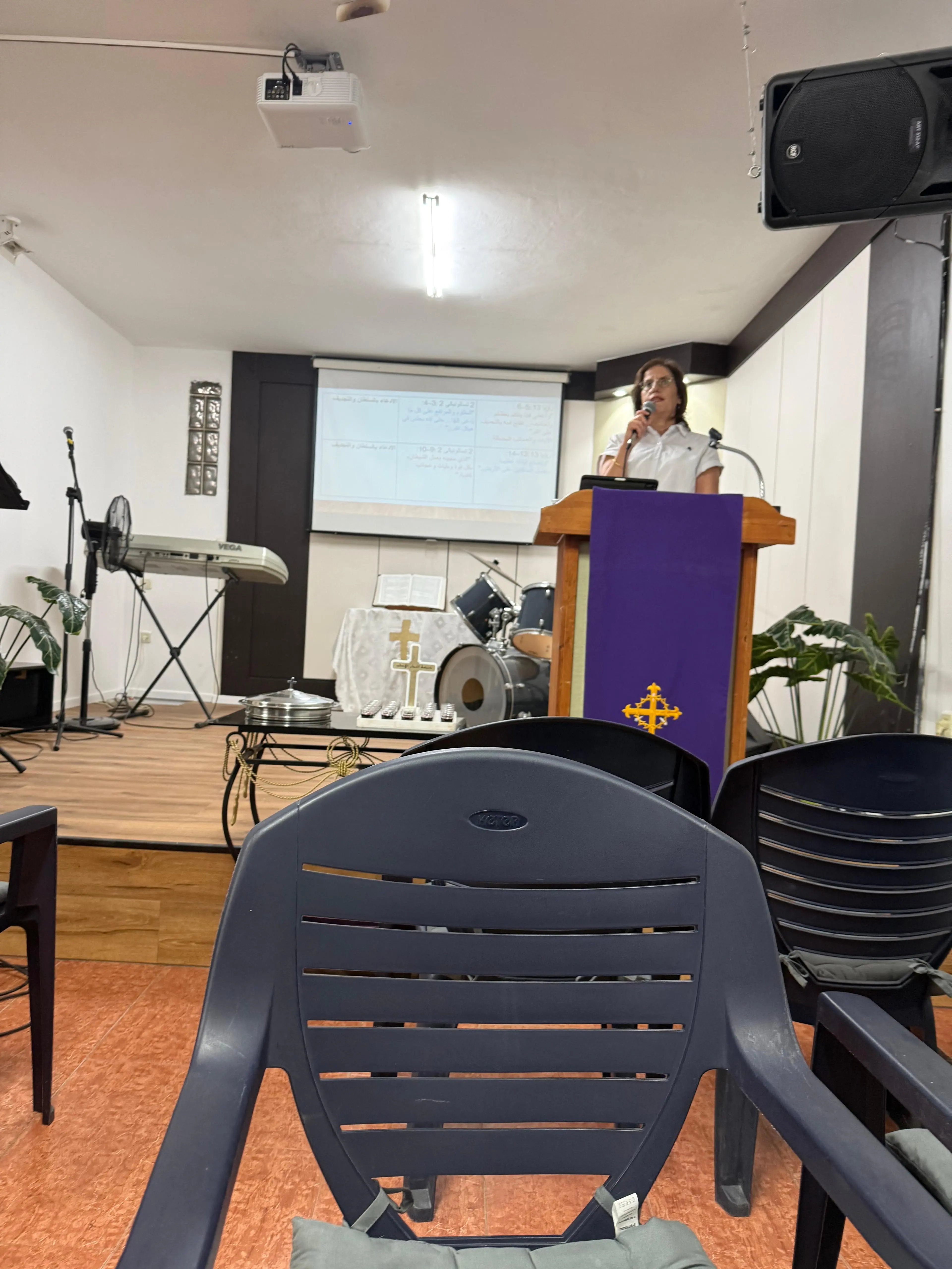 A woman preaching from the wooden pulpit with a purple banner bearing a gold cross